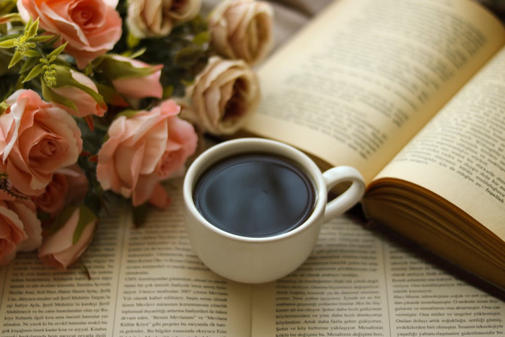 A serene still life featuring a coffee cup, open books, and blooming roses.